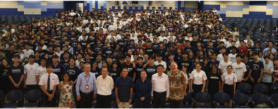 Large group of students and staff posing for a photo in an auditorium, many wearing navy Saints shirts.