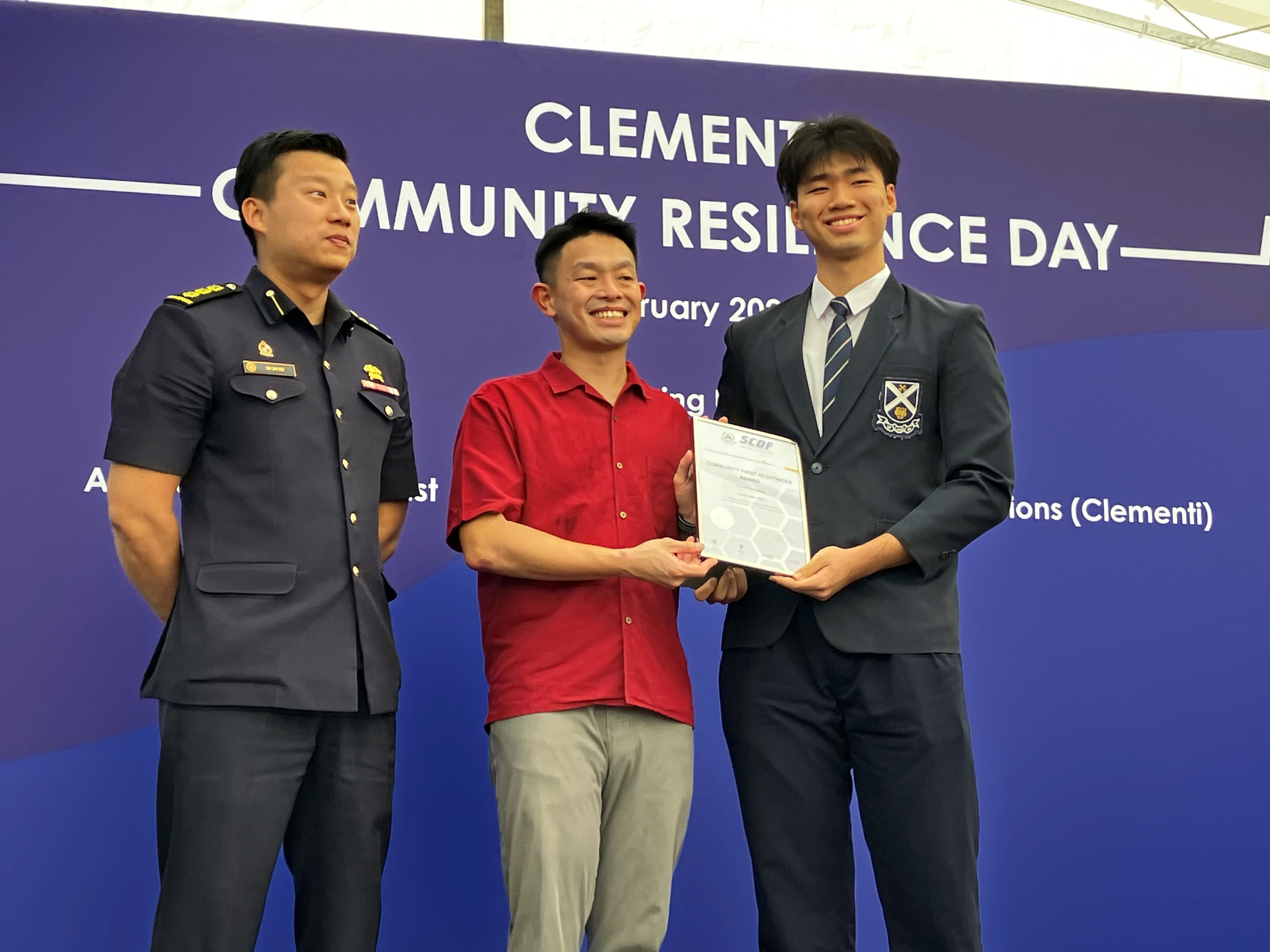 Three men smile while two hold a certificate at the Clementi Community Resilience Day event backdrop.