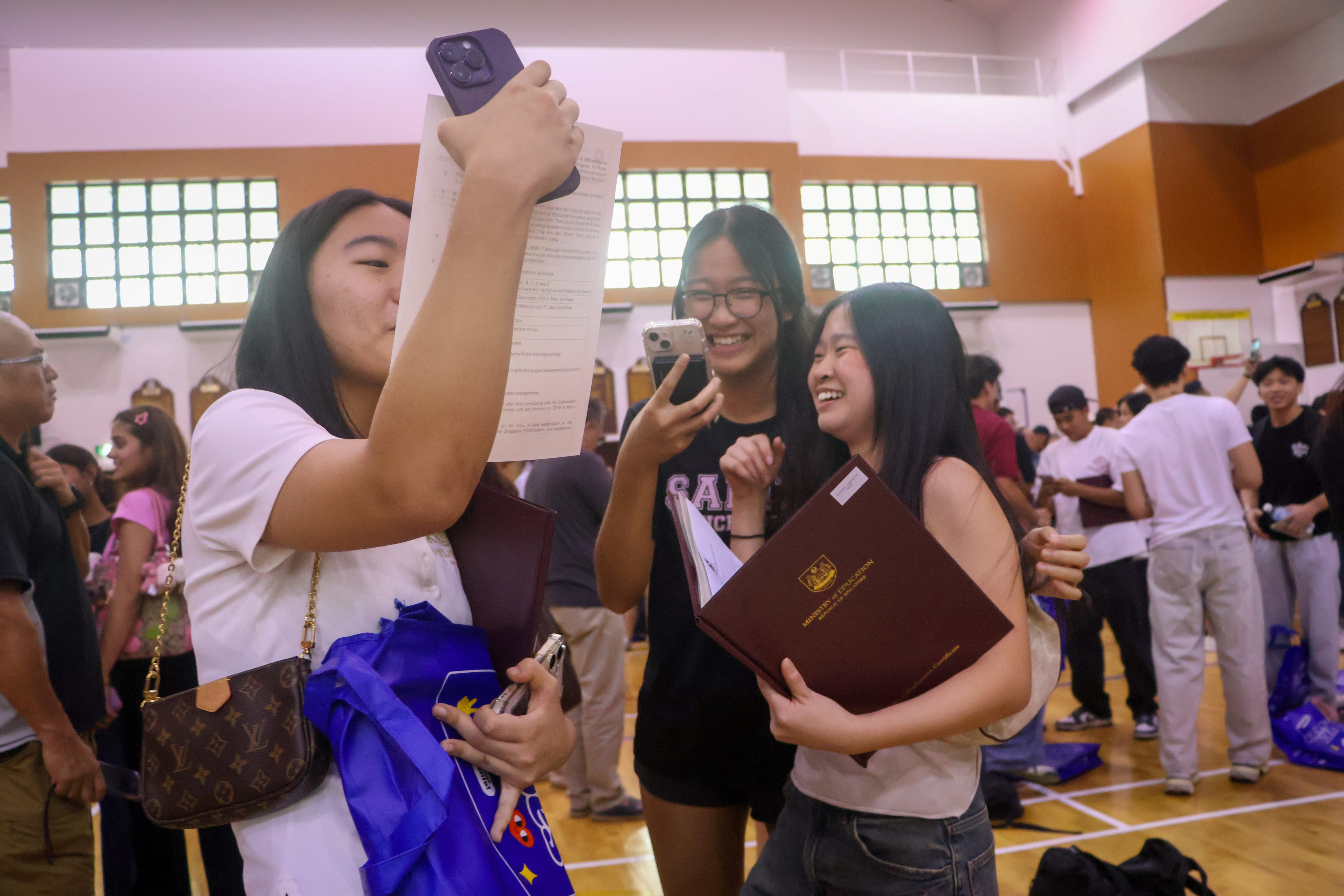 3 friends smiling and reviewing their A Level results in the hall.