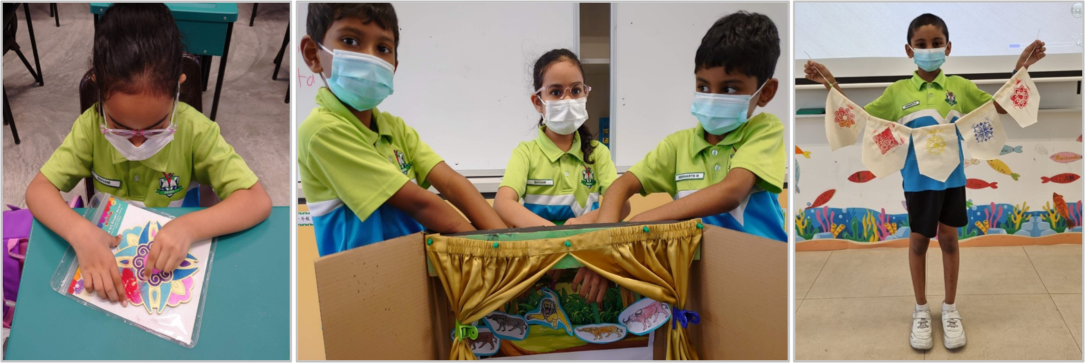 Three masked students in green uniforms doing classroom crafts, including a puppet theater box and a decorative fabric banner.