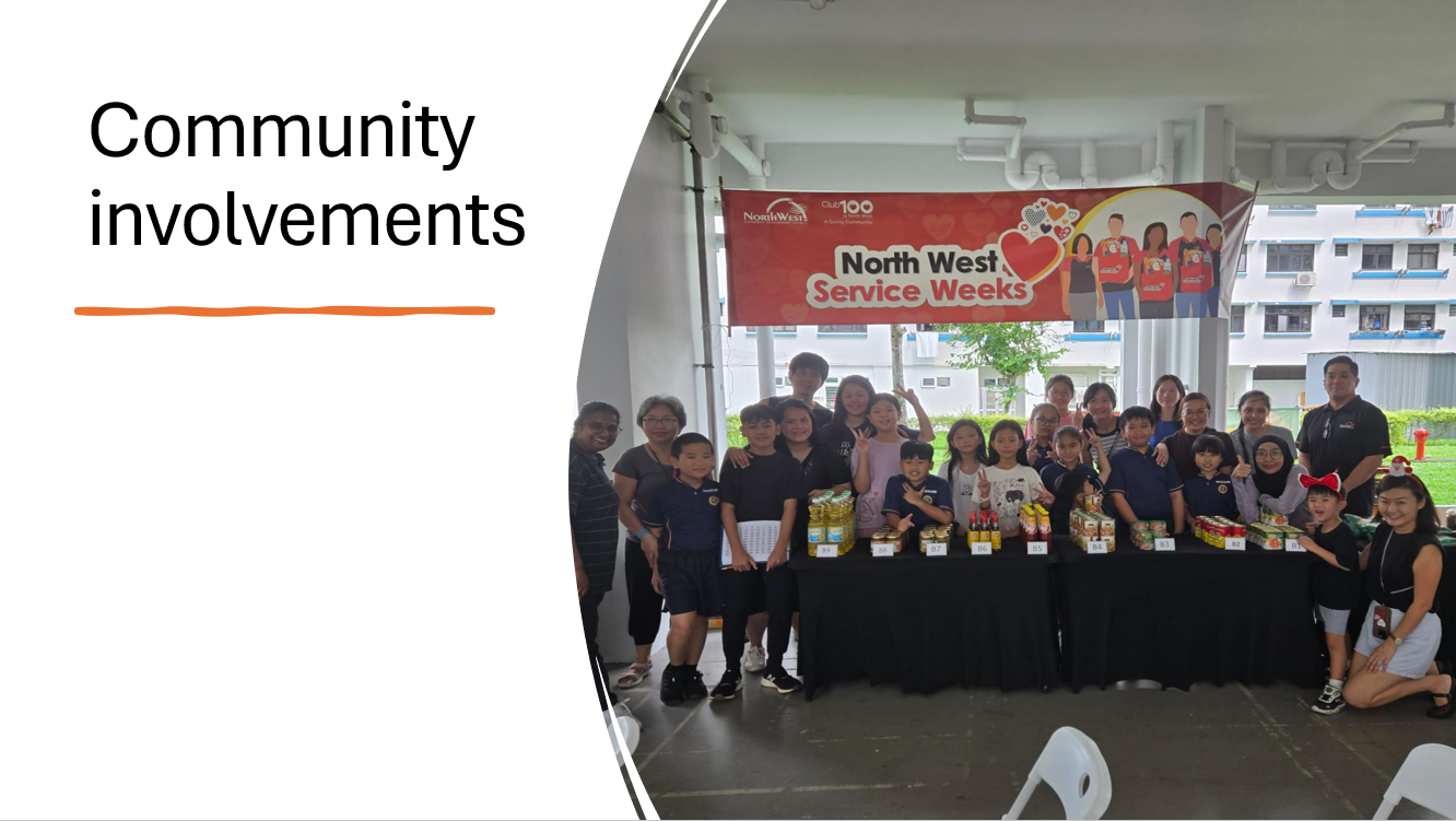 A group of adults and children pose at a North West Service Weeks community event with food items on a table.