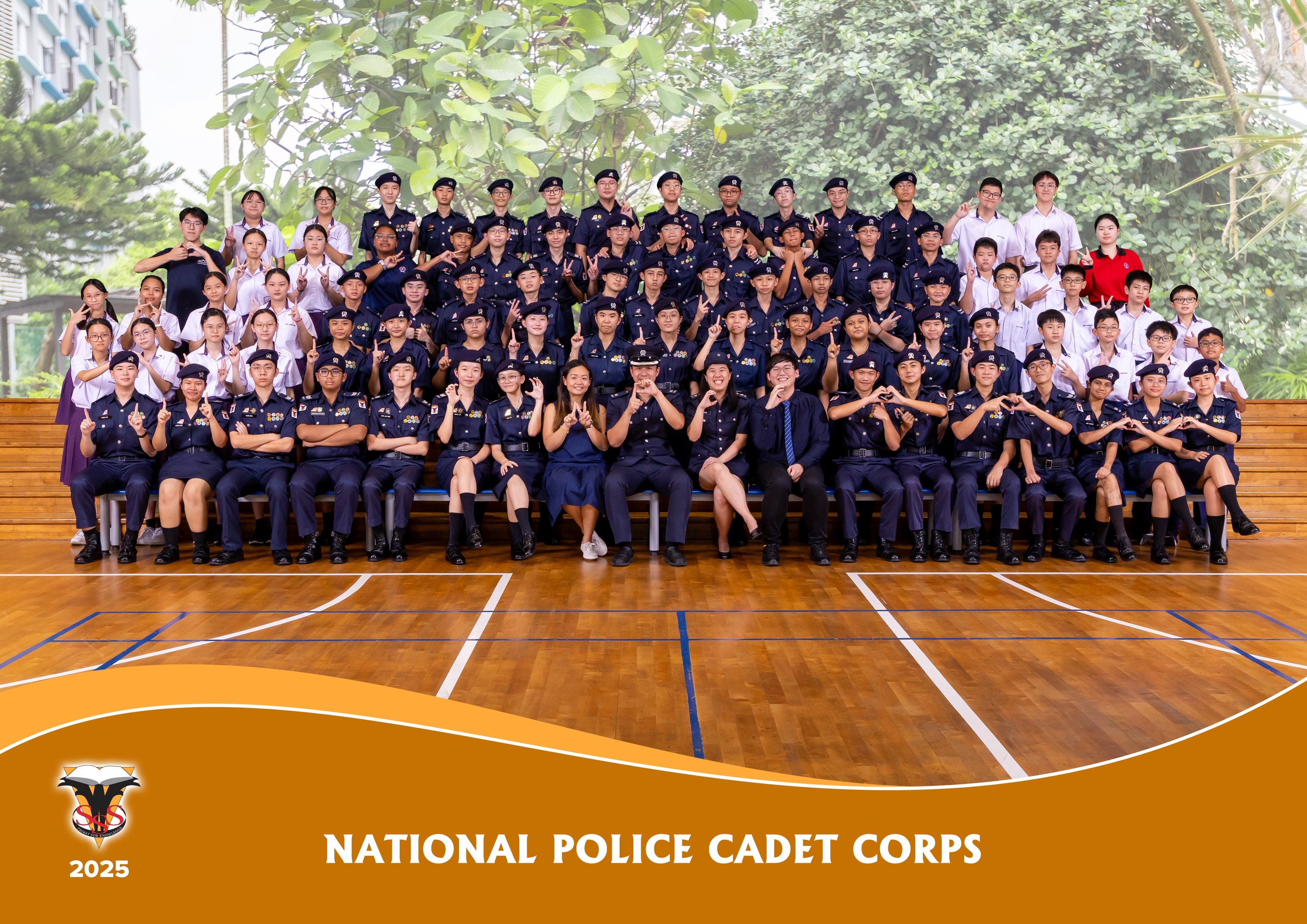 Group photo of National Police Cadet Corps 2025 members in navy uniforms posing in a school gymnasium.