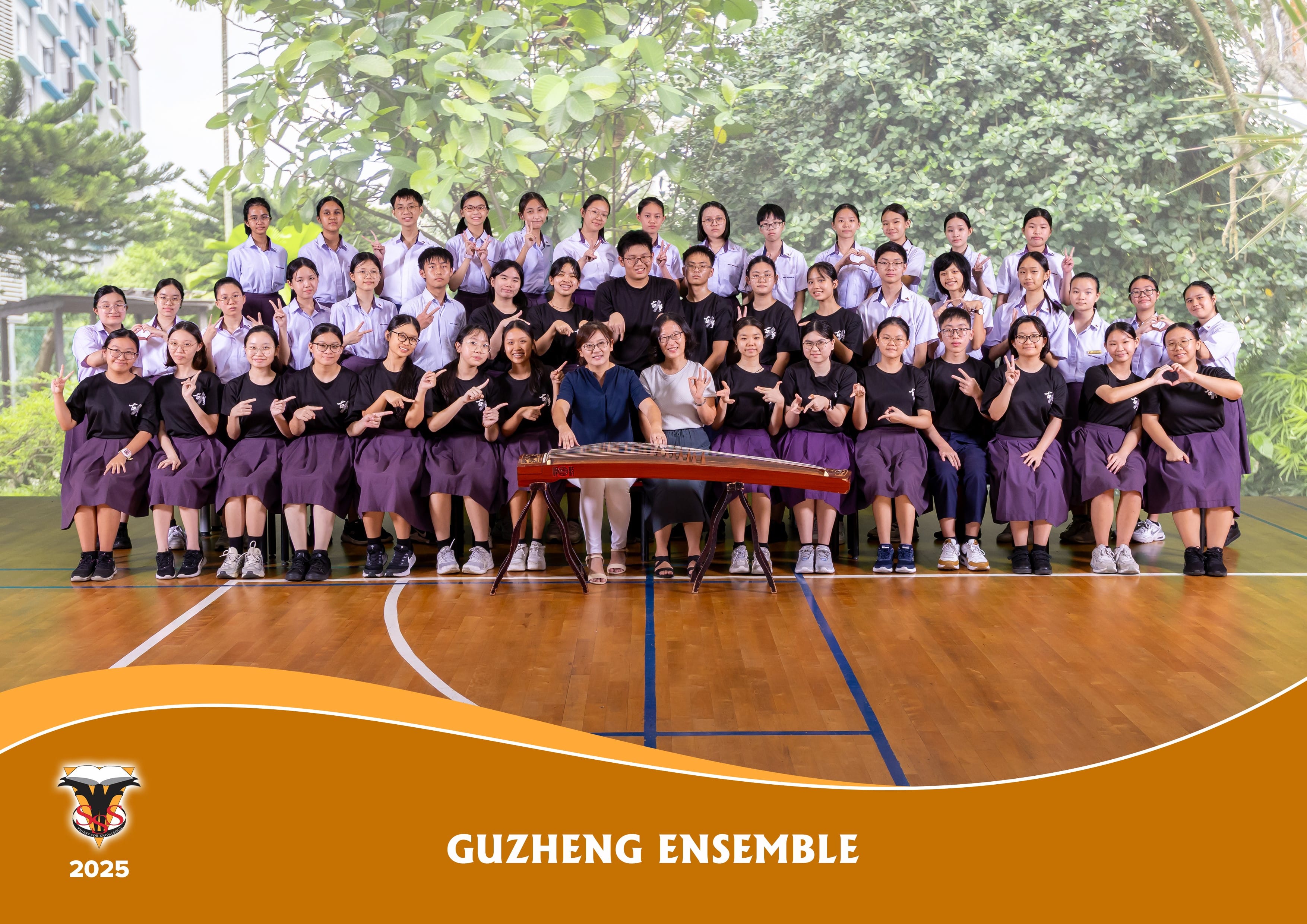 Group photo of a school Guzheng Ensemble 2025, students in uniform posing with a guzheng instrument on a gym floor.