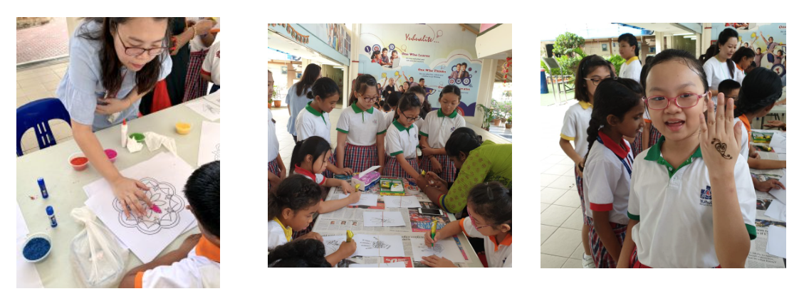 Students in school uniforms doing art activities at tables, with a girl waving and showing a hand tattoo.