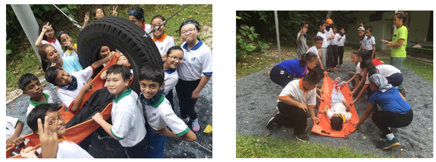 Children outdoors doing activities: posing near a large tire with a stretcher, and practicing carrying a person on a stretcher.