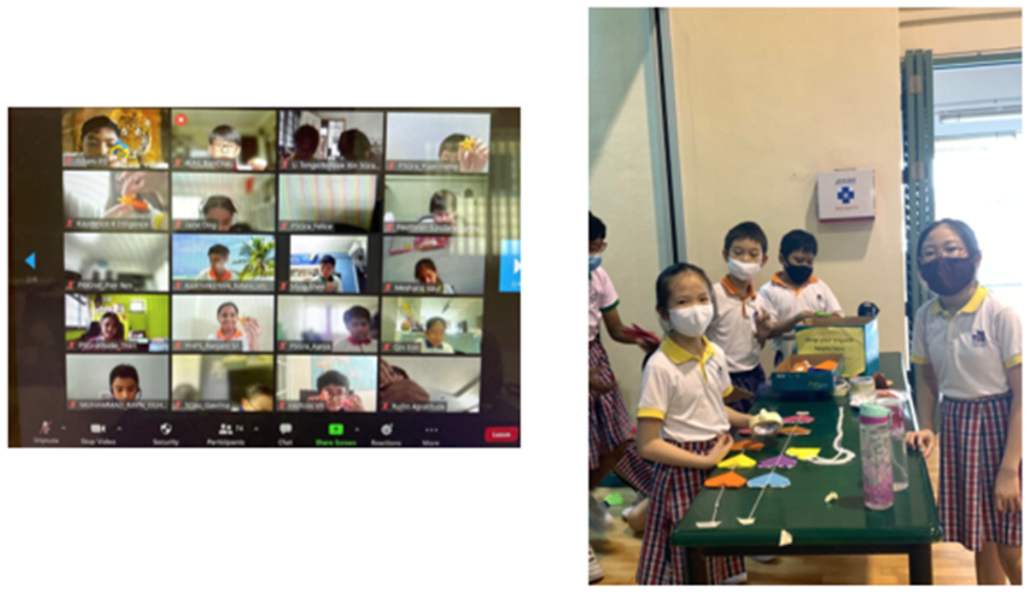 Students in masks stand by a table with paper crafts, beside a screen showing a Zoom call with many children.