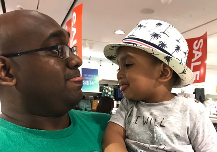 Father holding and smiling at a young child wearing a patterned hat in a shop