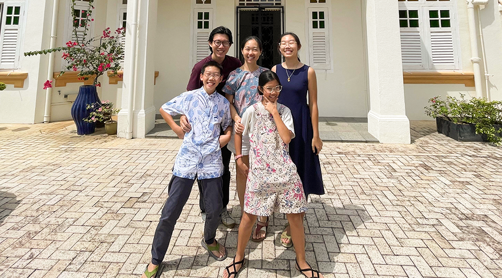 Family posing together outside a white heritage-style house on a sunny day