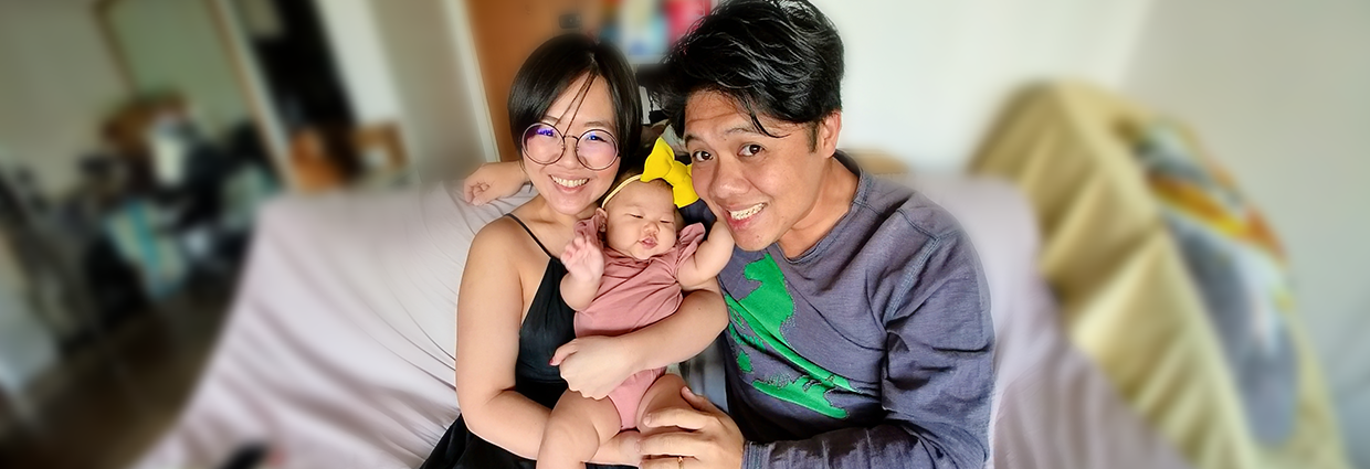 Parents smiling while holding their baby on a sofa at home