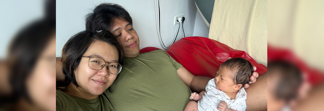 Parents relaxing on a sofa while holding and looking at their newborn baby