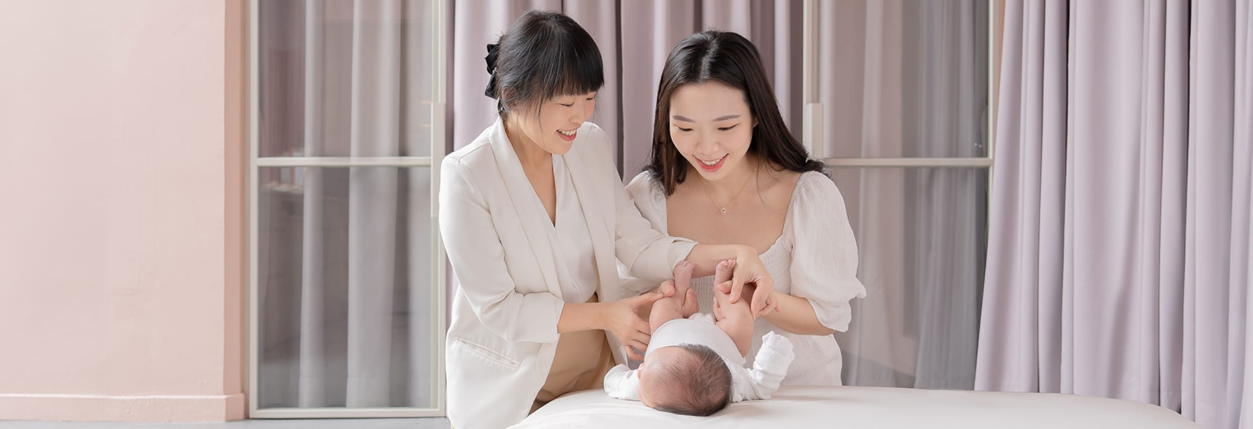 Two women smiling while caring for baby on changing table indoors