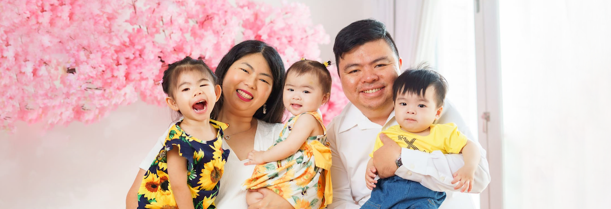 Family of four smiling together indoors beside pink blossom decorations