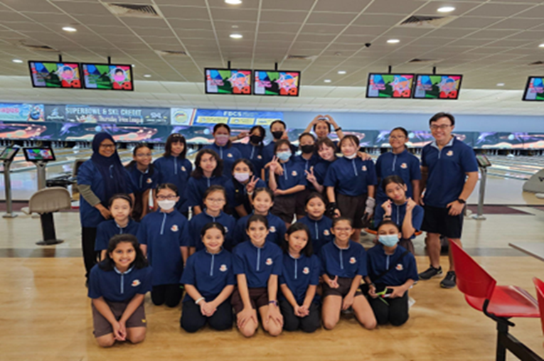 A large group of young students in matching navy uniforms pose together at a bowling alley.