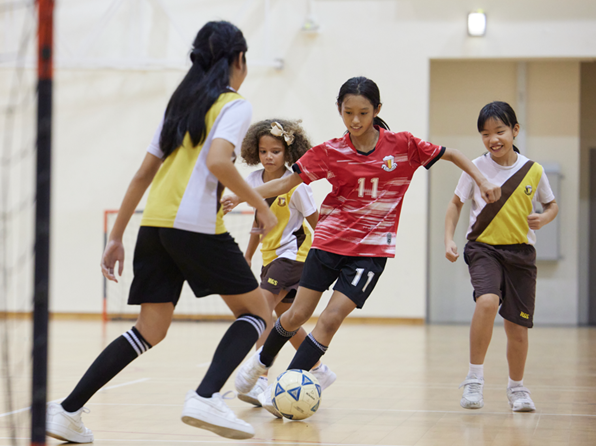 Four girls playing indoor soccer, with one in a red number 11 jersey dribbling the ball.