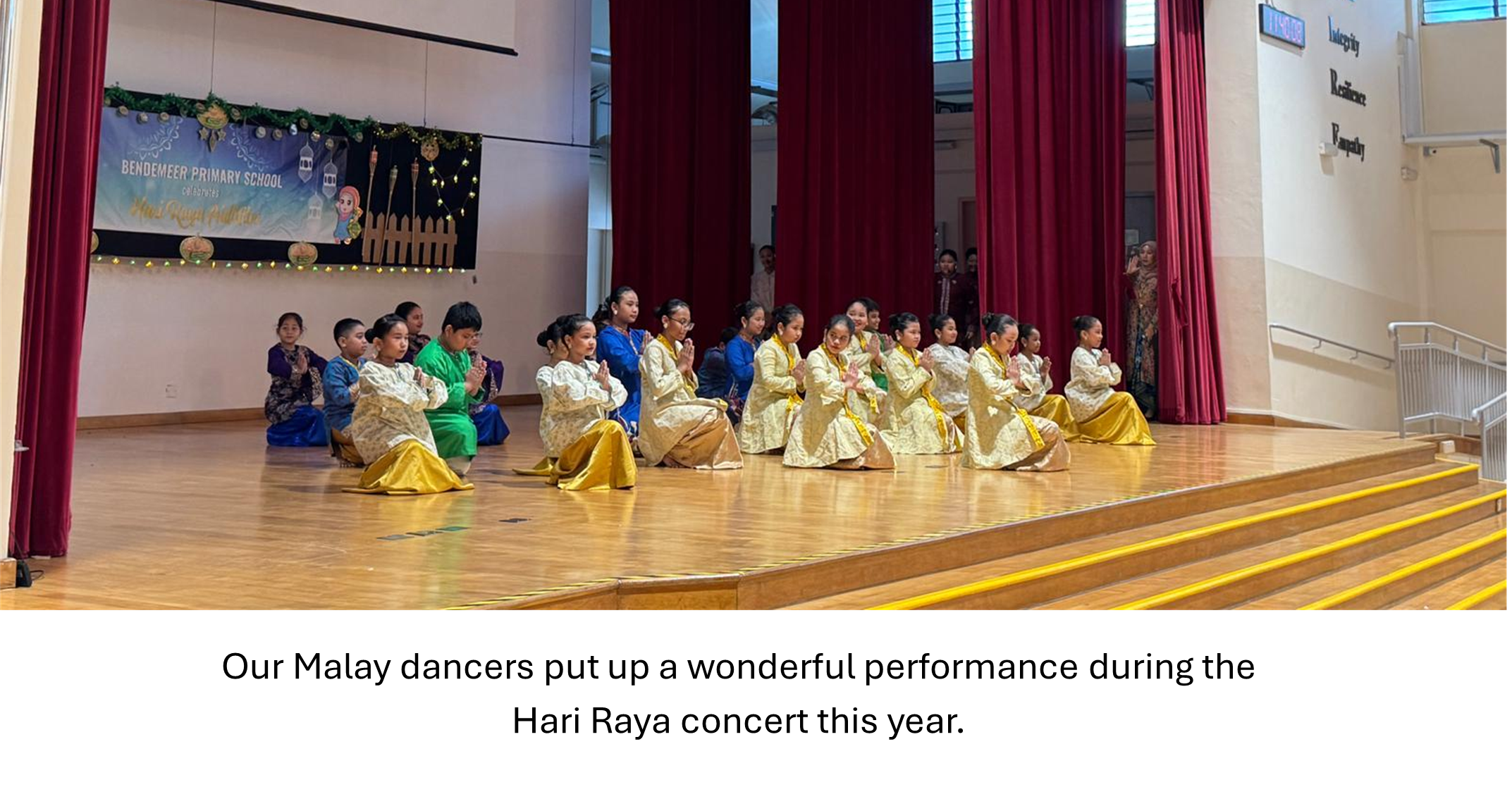 Children in gold and colorful traditional Malay costumes performing on a school stage during a Hari Raya concert.