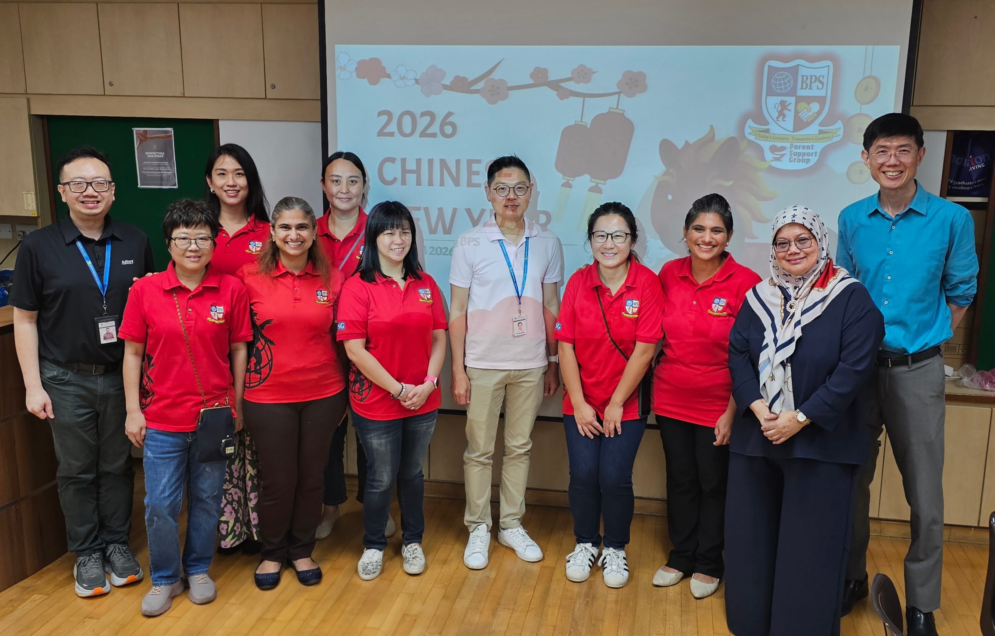 Group of eleven people posing indoors in front of a 2026 Chinese New Year BPS Parent Support Group projection screen.