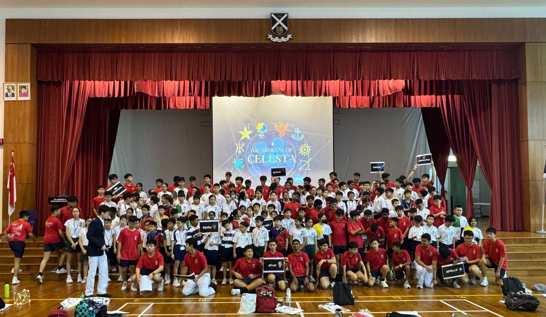 Large group of students posing in a school hall before a screen displaying "Guardians of Celesta."
