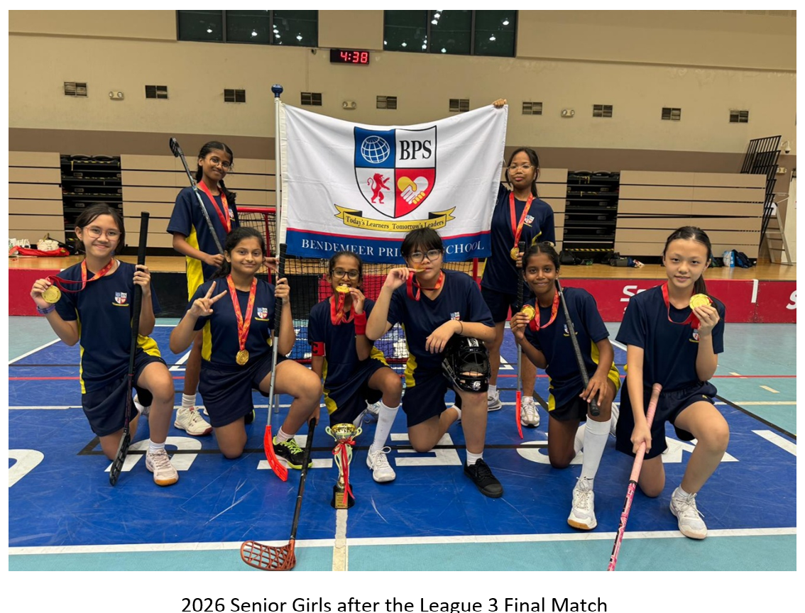 Eight girls in navy uniforms hold gold medals, floorball sticks, and a BPS school flag on an indoor court.