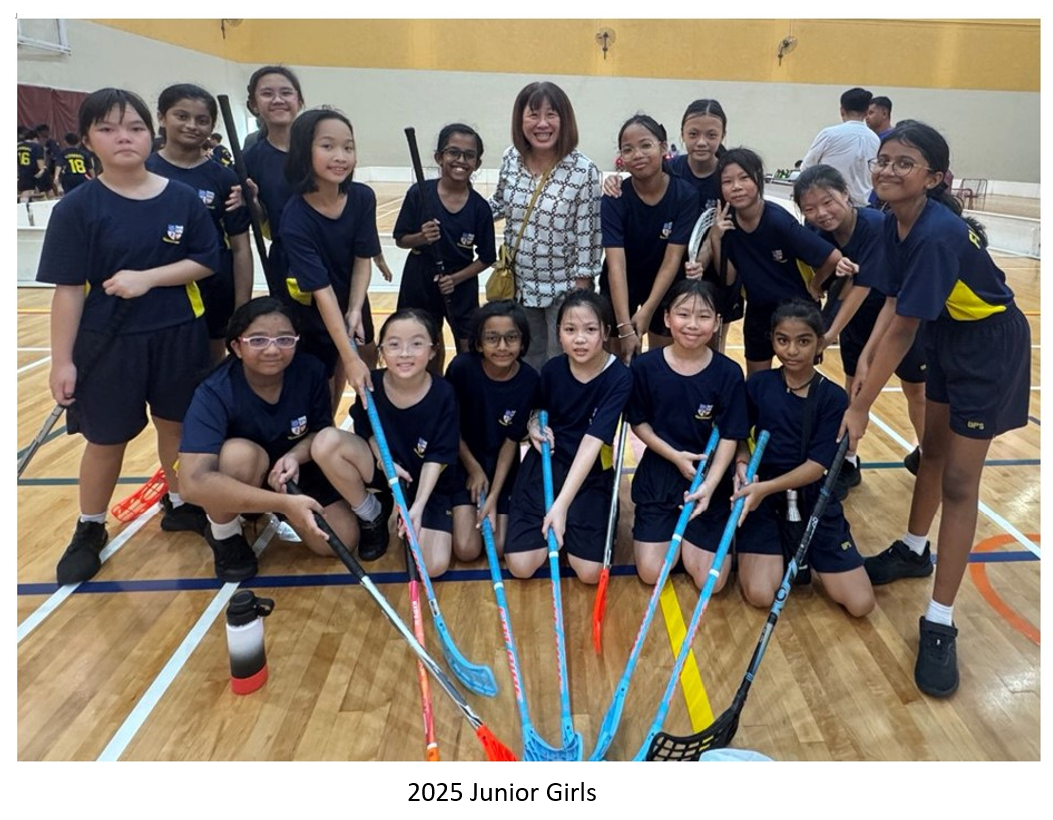 Group of junior girls posing with floorball sticks on an indoor court with Principal