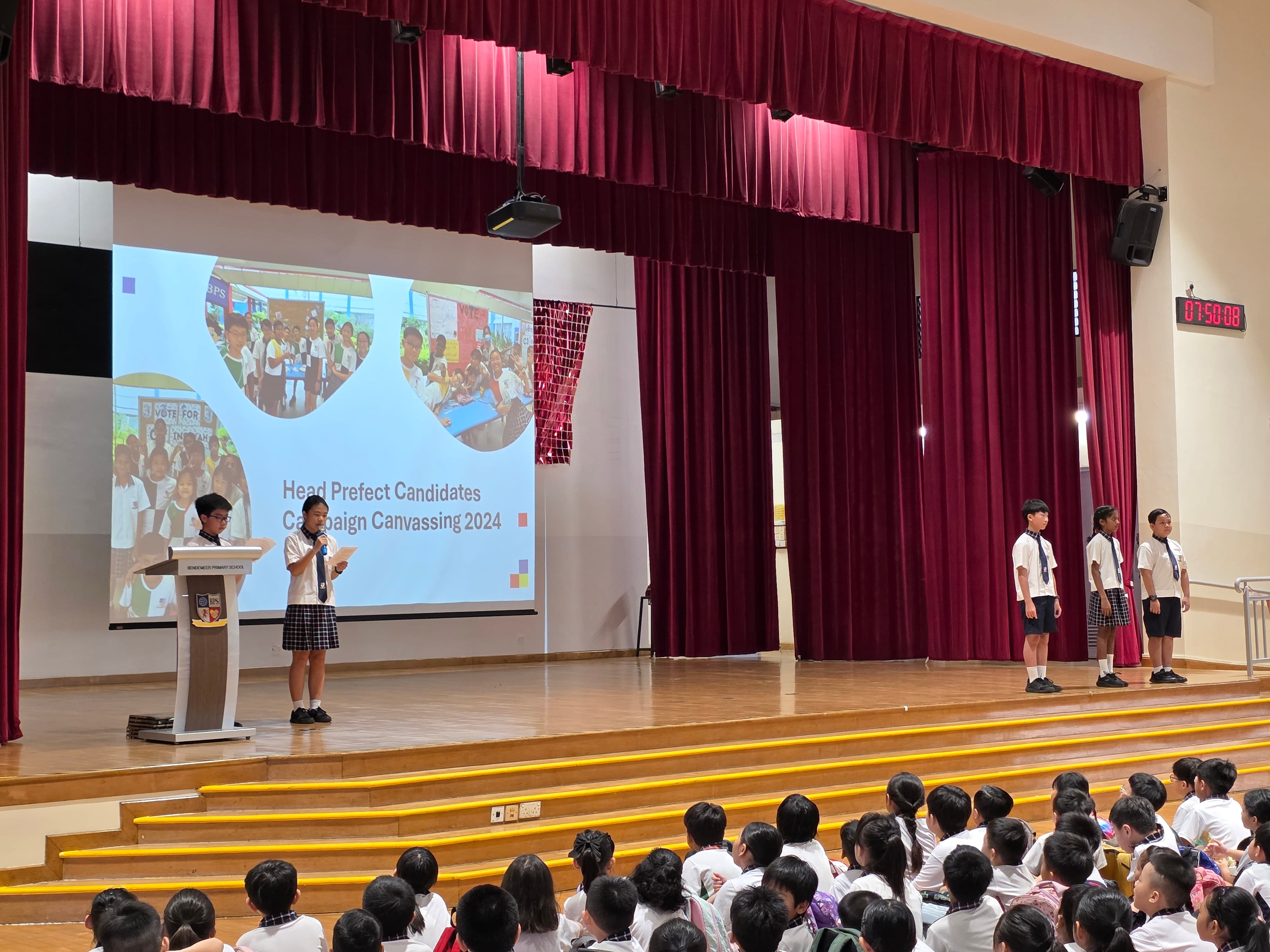 A student speaks at a podium on stage during a Head Prefect Candidates Campaign Canvassing 2024 school event.