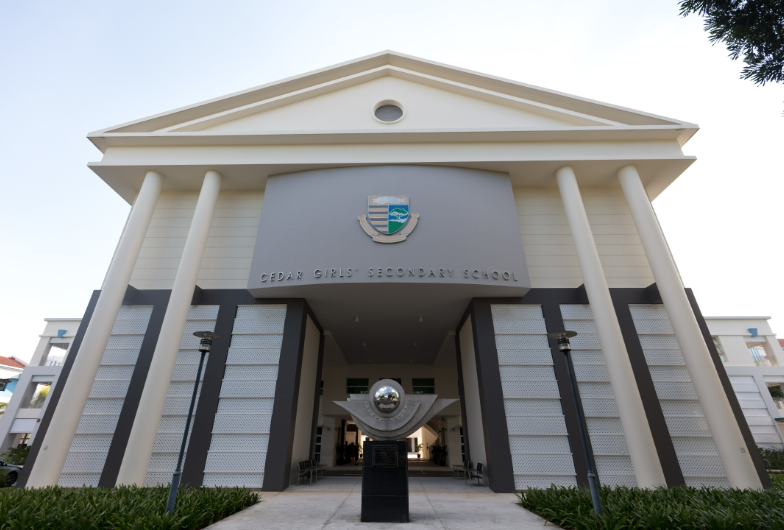 Front entrance of Cedar Girls' Secondary School with white columns, triangular pediment, crest, and a sculpture below.