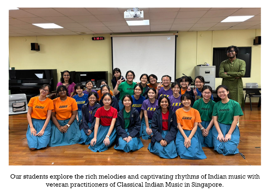 A group of students in colorful t-shirts and blue skirts pose together in a classroom with a projector screen.
