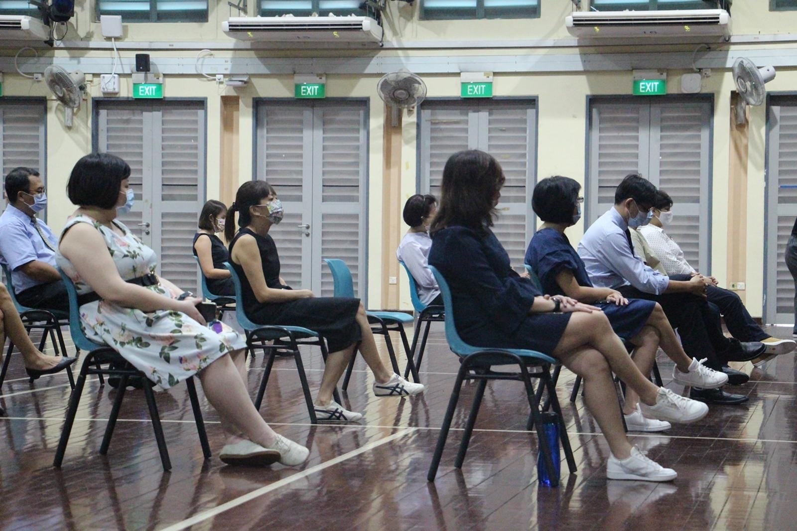 School Staff wearing face masks seated apart in the school auditorium