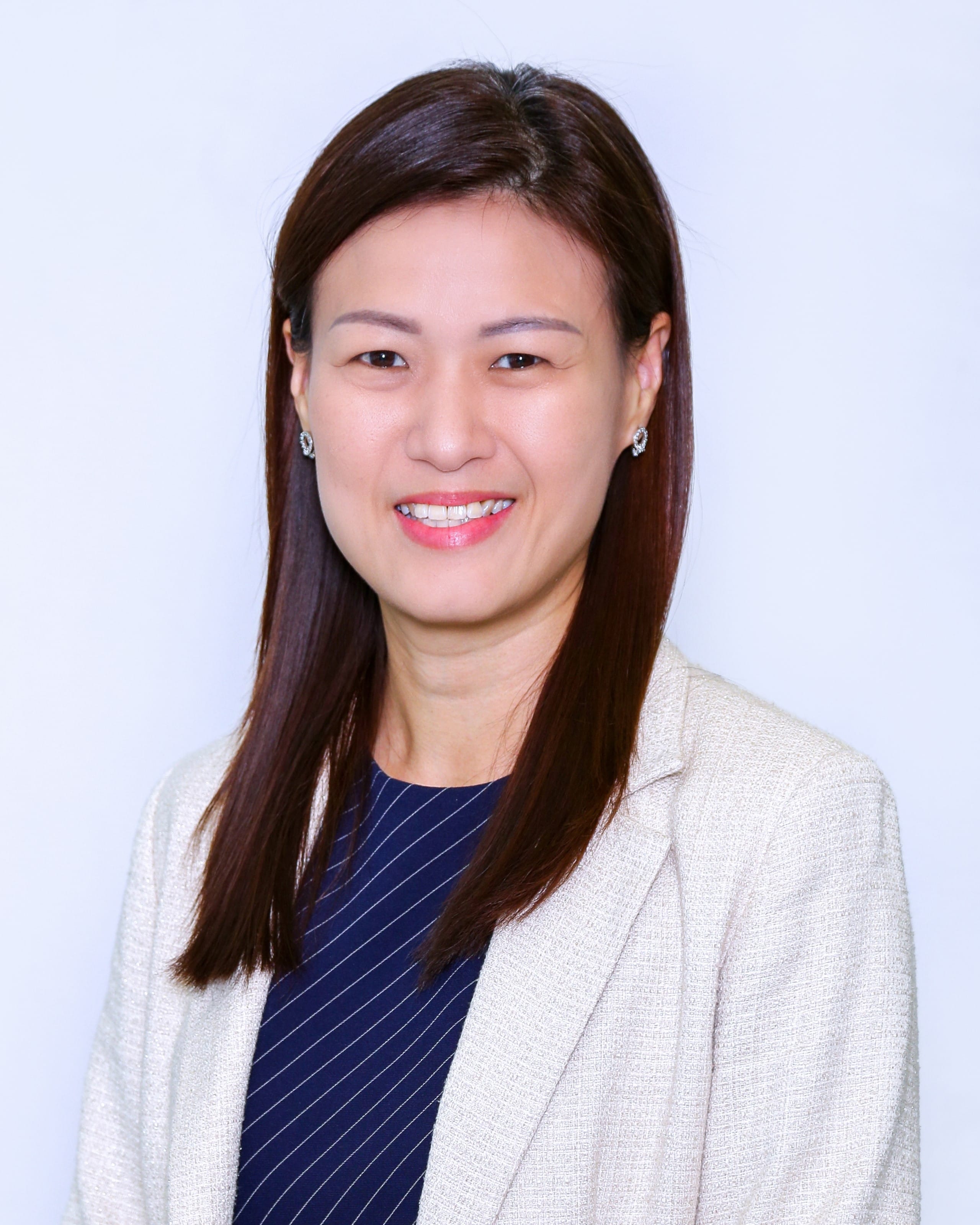 A smiling woman with long dark hair wearing a beige blazer and navy striped top against a light background.
