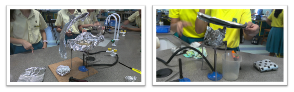 Students in uniforms work on science projects with foil, tubes, and containers on classroom tables.