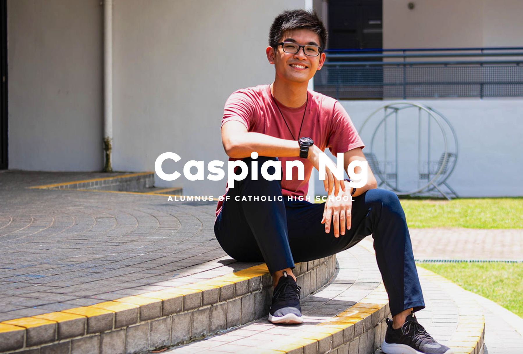 Young man with glasses and a red shirt sits smiling on outdoor steps, labeled Caspian Ng, Alumnus of Catholic High School.