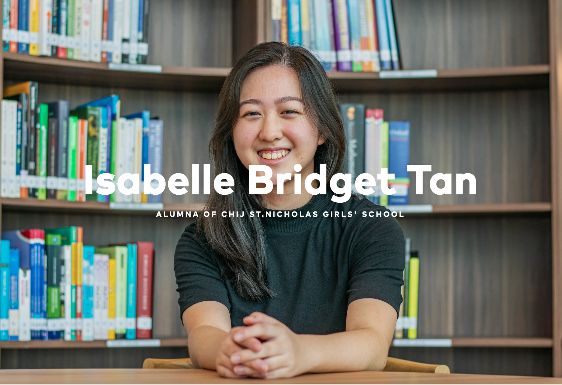 Smiling person seated at a table in front of bookshelves, with text Isabelle Bridget Tan across the center.