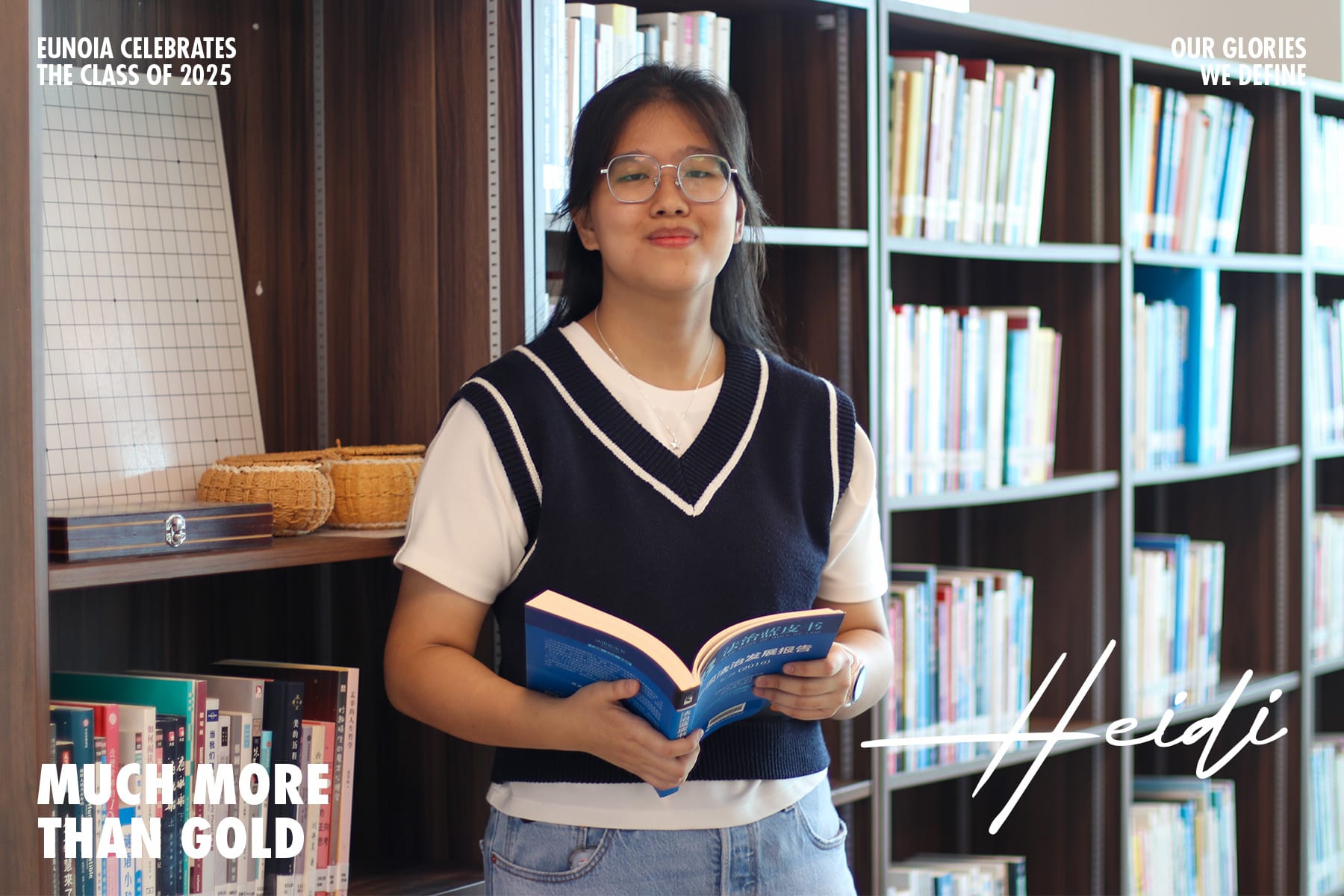Young woman named Heidi wearing glasses holds an open book, smiling in a library with shelves of books behind her.