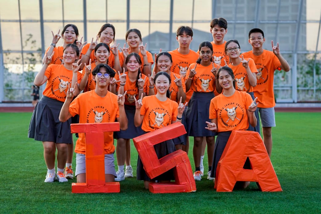 Group of students in orange Junior College shirts pose on a field with large orange letters I, E, A.