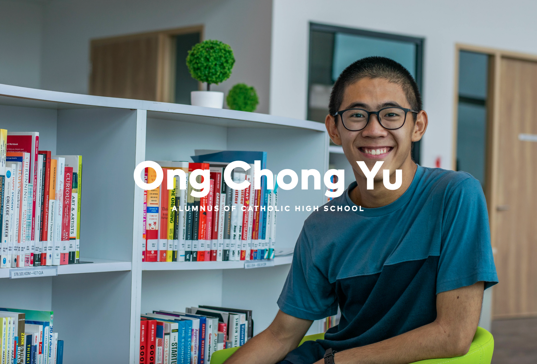 Smiling young man with glasses sits in front of a white bookshelf, labeled Ong Chong Yu, alumnus of Catholic High School.