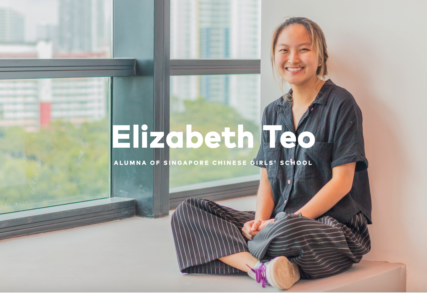 Elizabeth Teo, alumna of Singapore Chinese Girls' School, smiling and sitting cross-legged by a window.
