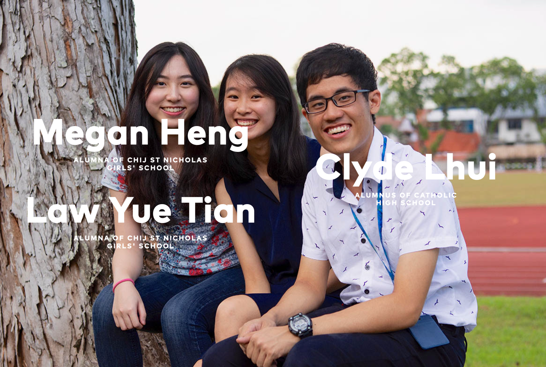 Three smiling young people, Megan Heng, Law Yue Tian, and Clyde Lhui, sitting together outdoors near a tree.