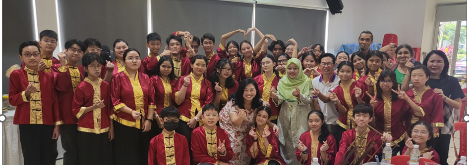 Large group of young people in red and gold uniforms posing indoors, making heart and peace signs.