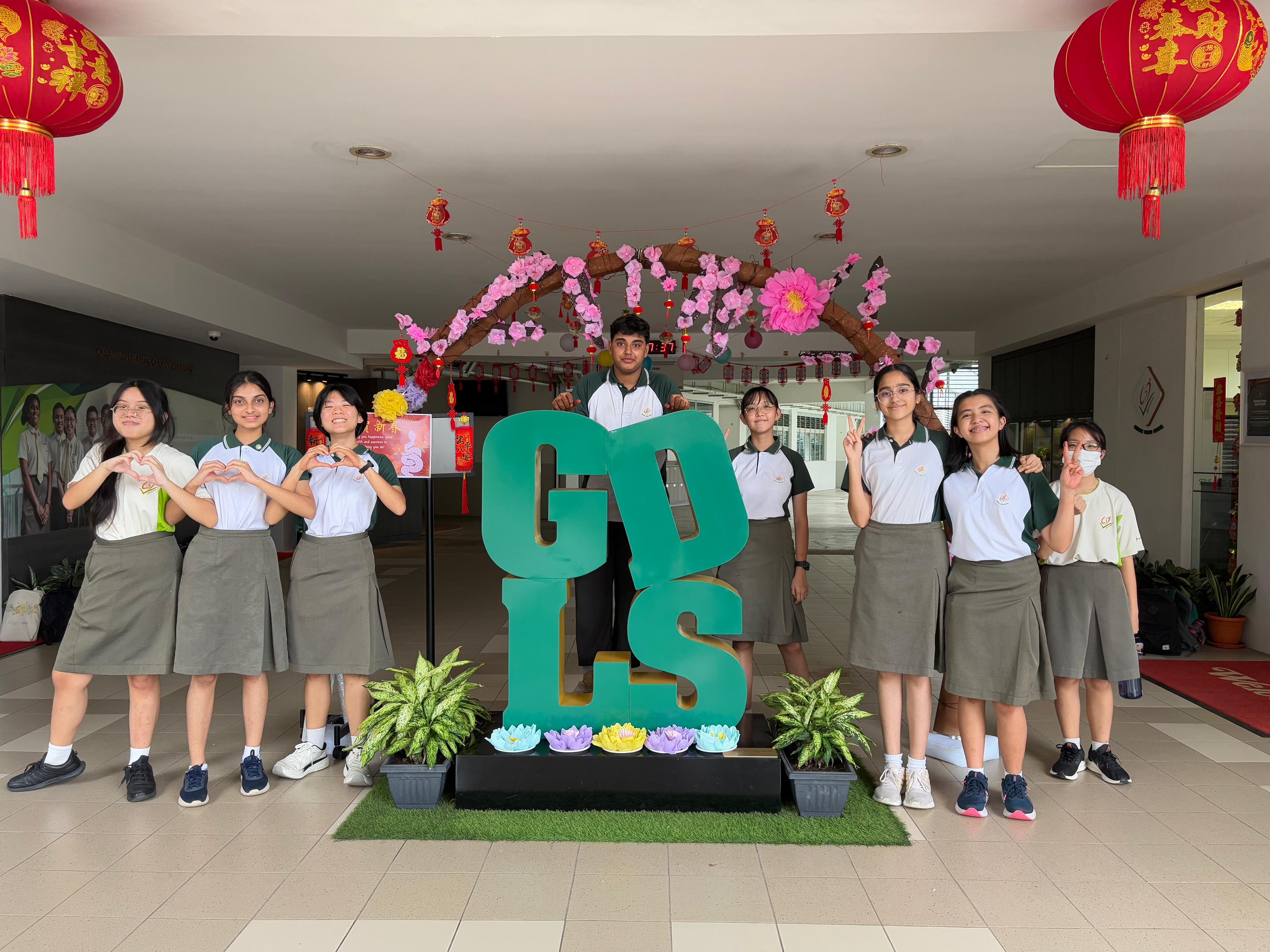 Seven students in uniforms pose around a green GDLS letter sign with Chinese New Year decorations and red lanterns.