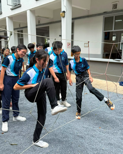 Students in school uniform navigating through a low ropes balance and web obstacle course outdoors.