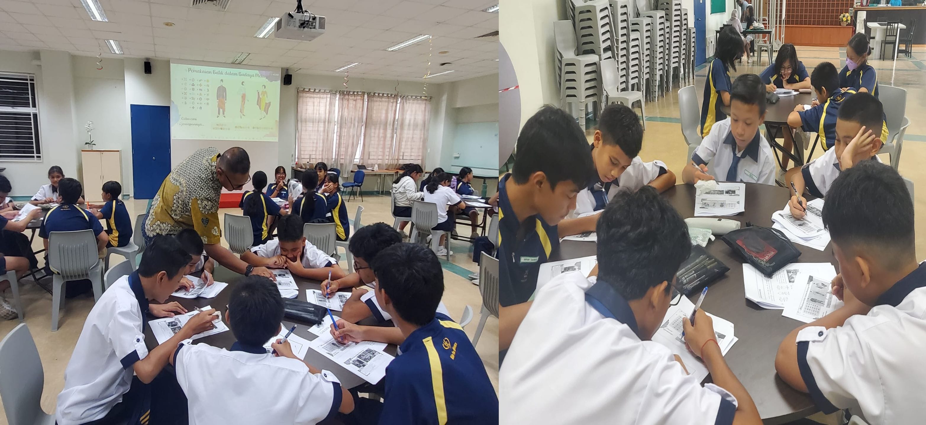 Students in blue and white uniforms work on worksheets at tables while a teacher assists, with a projected slide visible.
