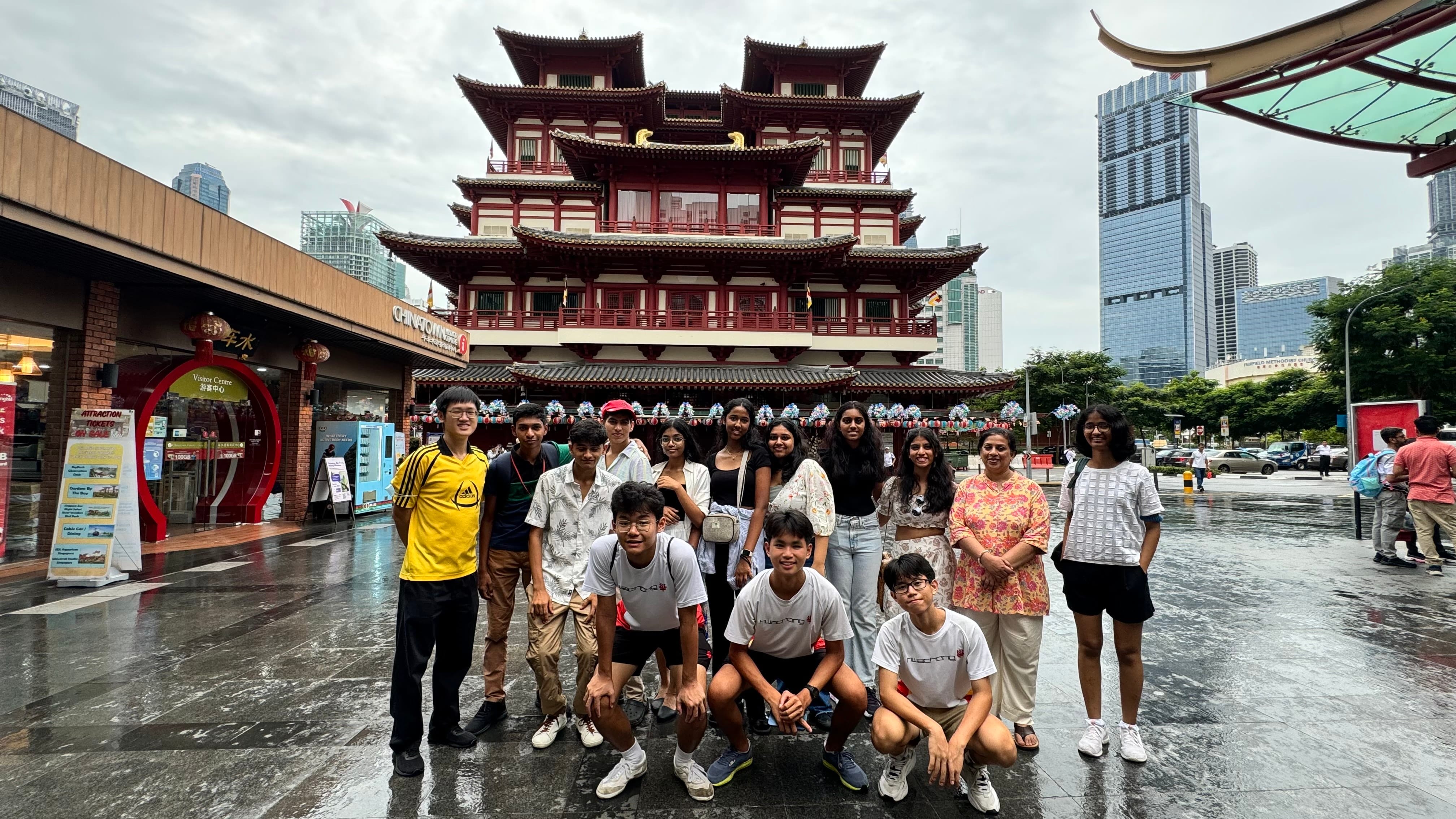 A group of teenagers poses on a wet street in front of a red multi-tiered Chinese temple in Singapore's Chinatown.