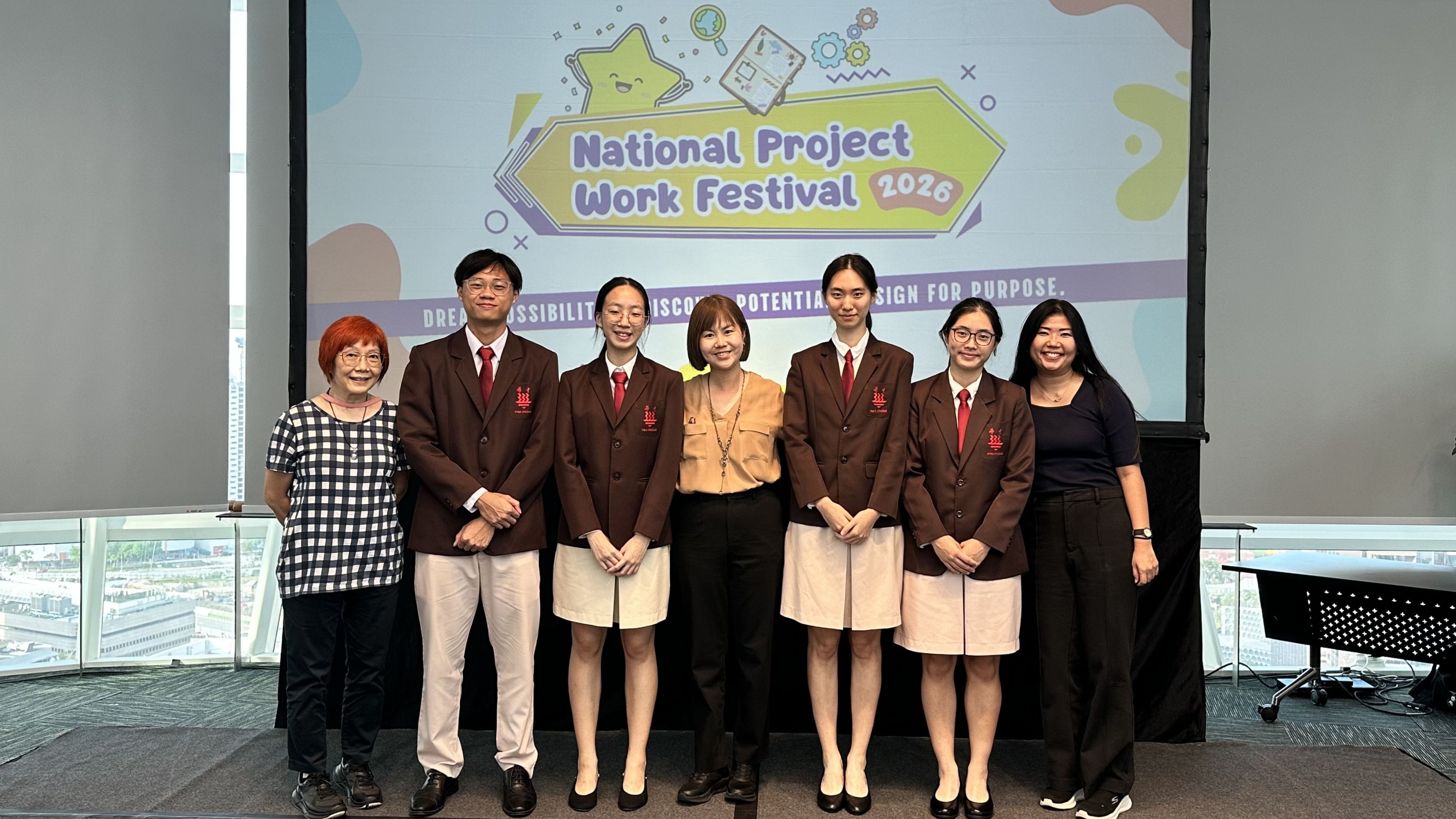 Seven people pose in front of a National Project Work Festival 2026 banner, four wearing brown school uniforms.