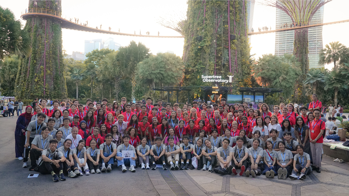 A massive group photo of all summit delegates wearing red and grey shirts, posing outdoors in front of the Supertree Observatory at Gardens by the Bay.