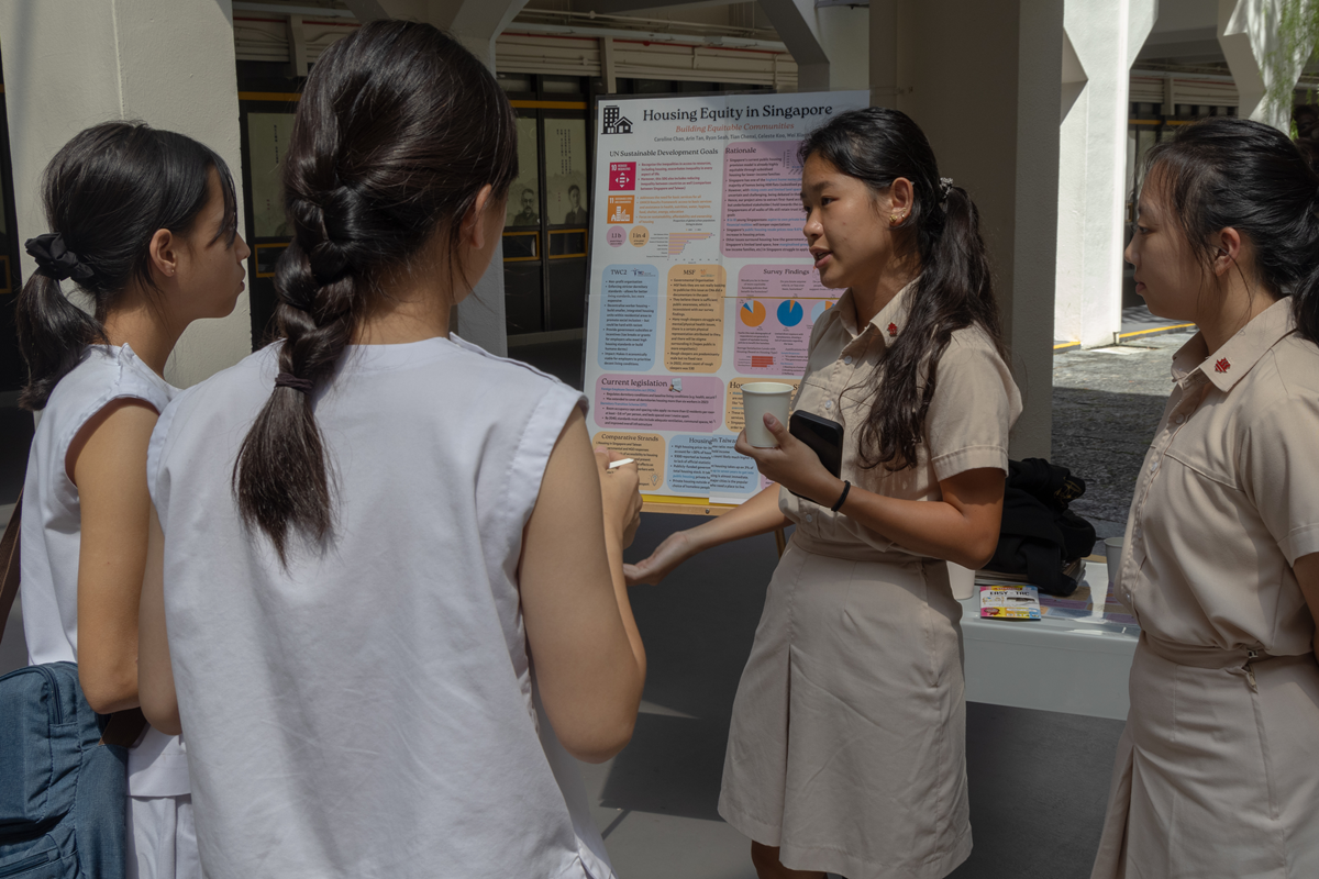 A student presents a poster titled Housing Equity in Singapore to three peers outdoors.
