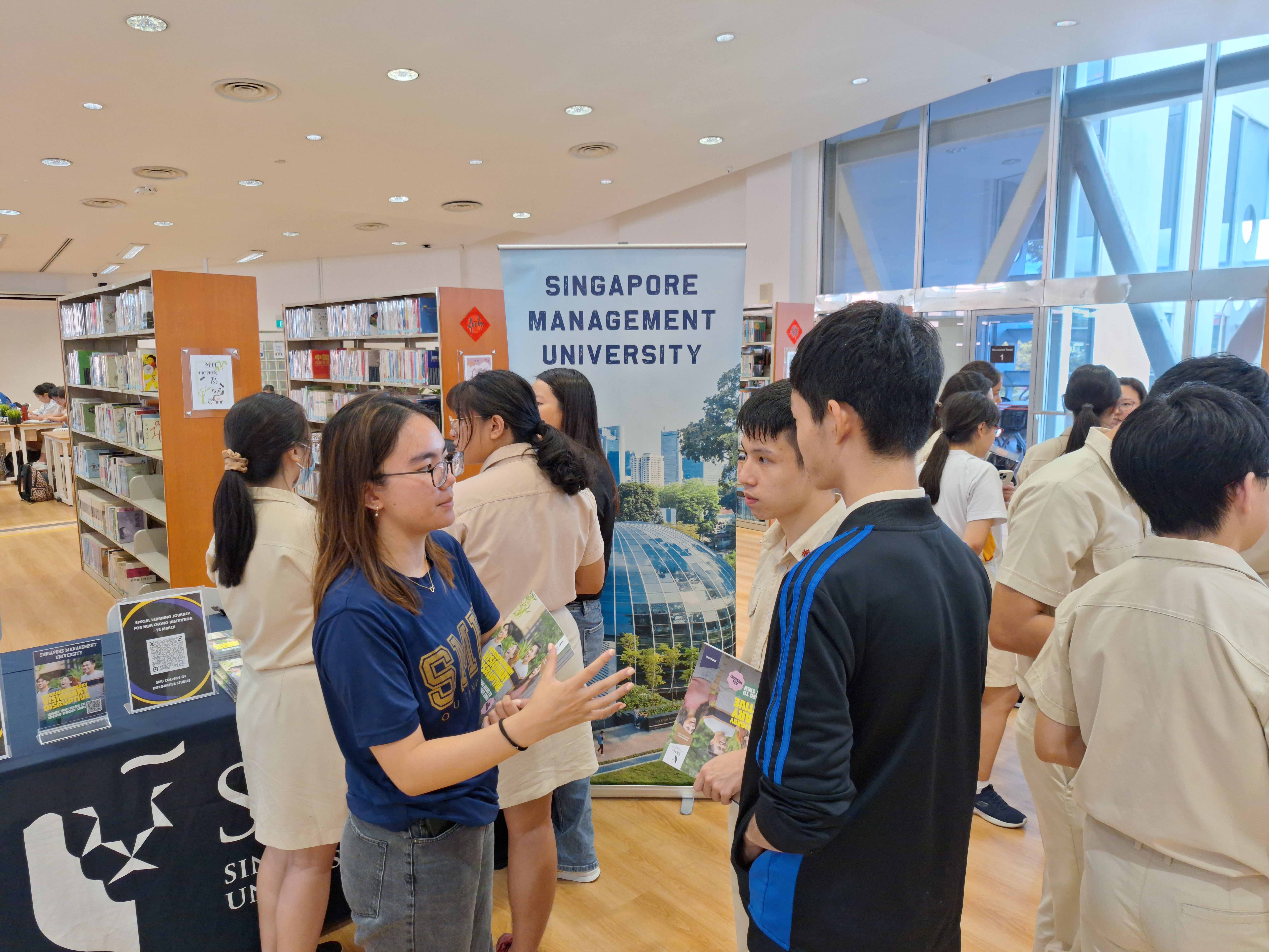 Student talks with visitors at a Singapore Management University booth inside a library.