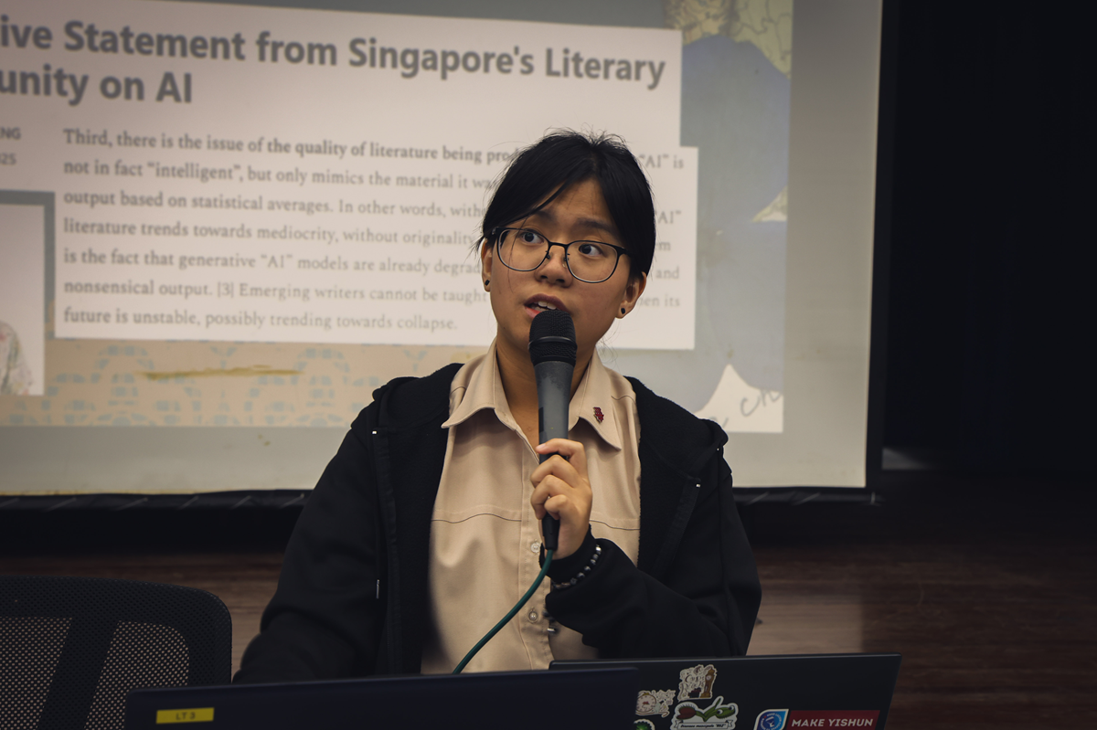 Young woman with glasses speaking into a microphone before a projected slide about Singapore's Literary Community on AI.