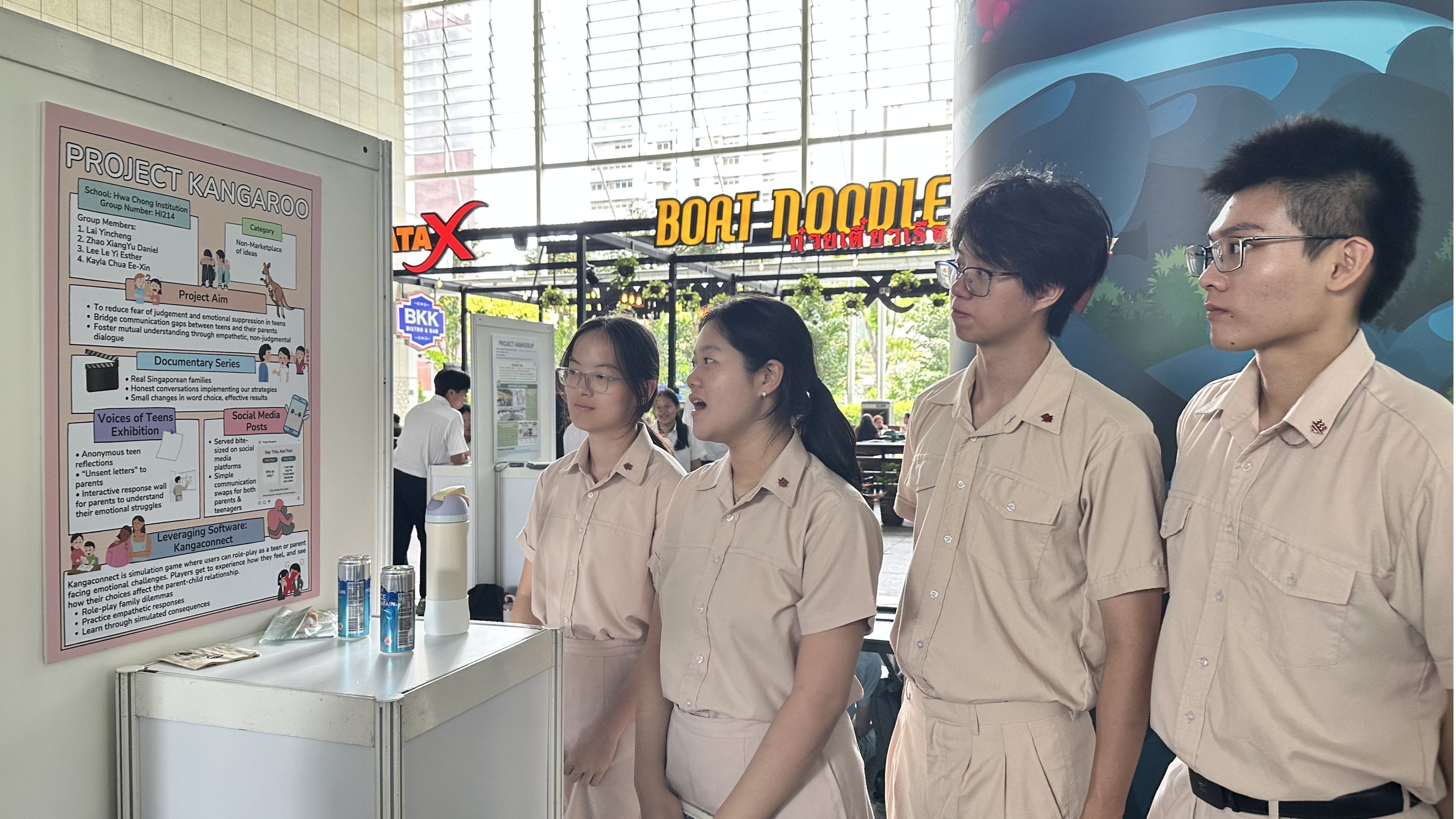 Four students in beige uniforms stand beside a poster board displaying their school project titled Project Kangaroo.
