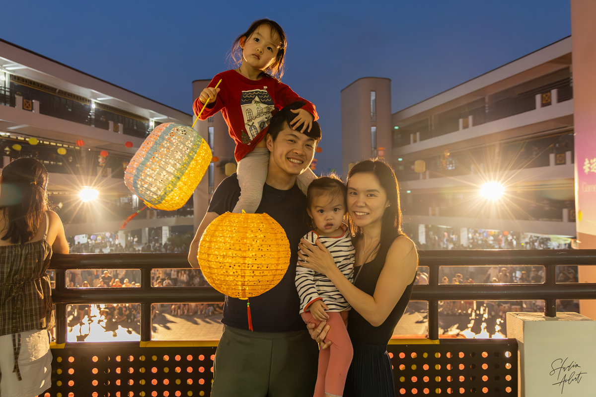 A family of four posing together on the bridge at dusk while holding traditional paper lanterns during the Mid-Autumn Festival.