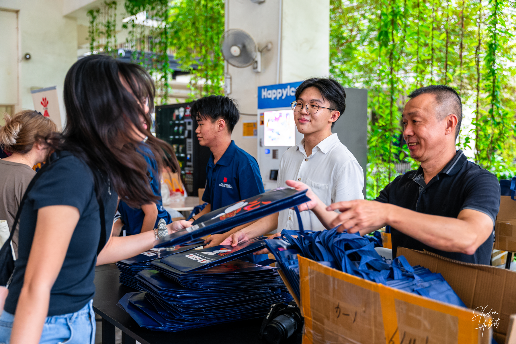 Man hands a folder to a woman at a table piled with blue folders and lanyards, with two others behind.