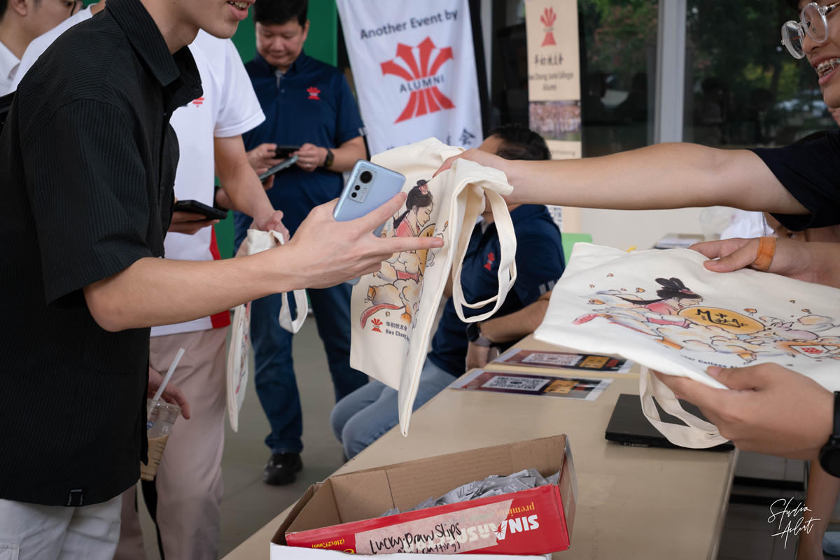 A close-up shot of students receiving illustrated MAF tote bag as a door gift at the registration counter.